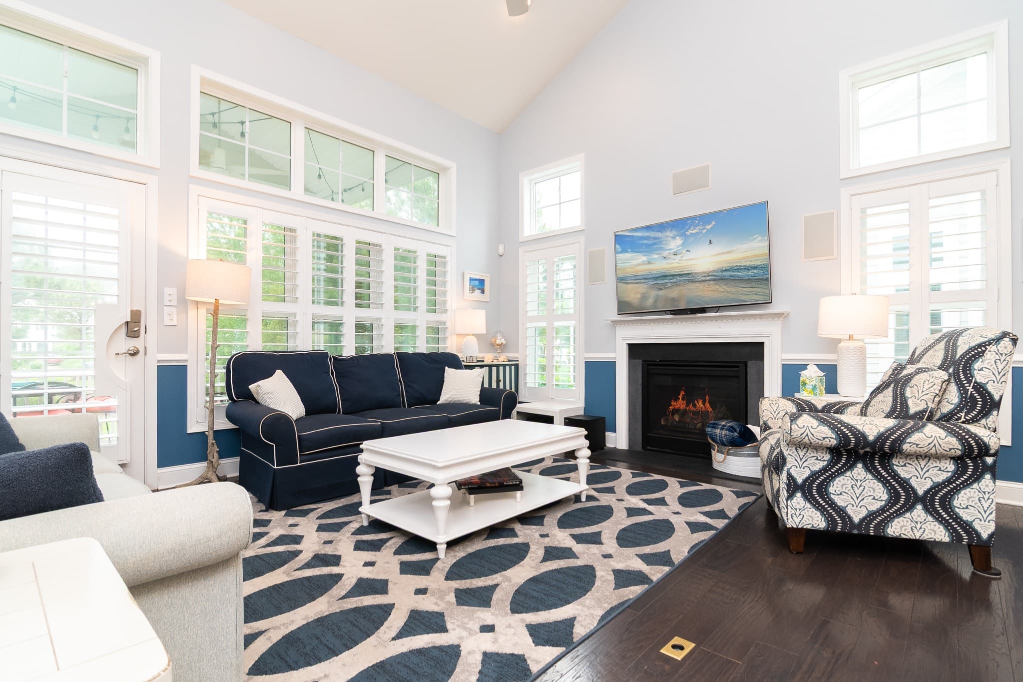 First-floor family room with two sofas, a reclining chair, large smart TV, a gas fireplace, and local artwork. The left sofa converts into a queen sofa bed.