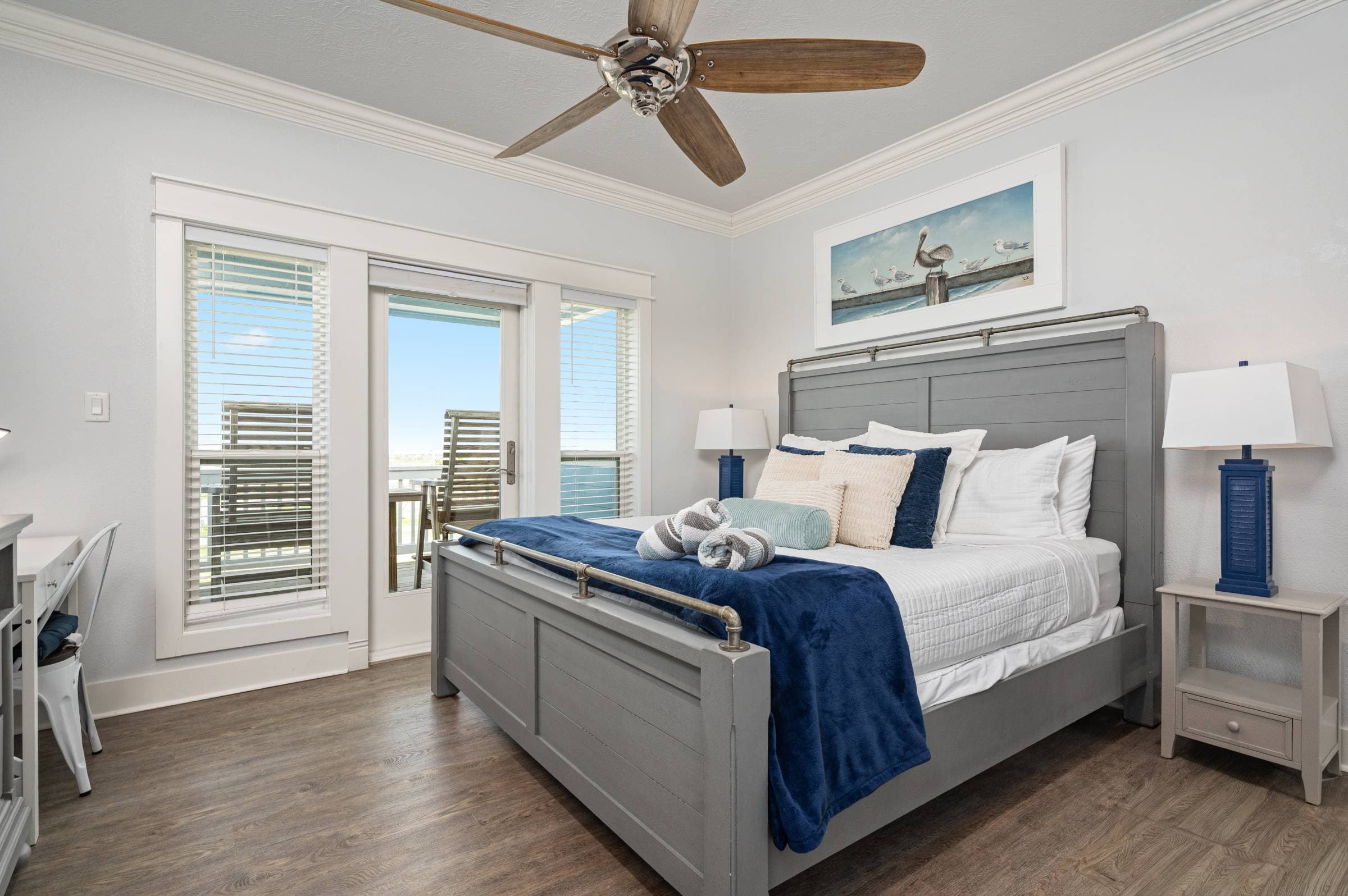 Bright top-floor bedroom with king bed, ensuite bath, smart TV, and desk. Step through the glass door to your private deck, which includes two chairs and a small table for relaxing.
