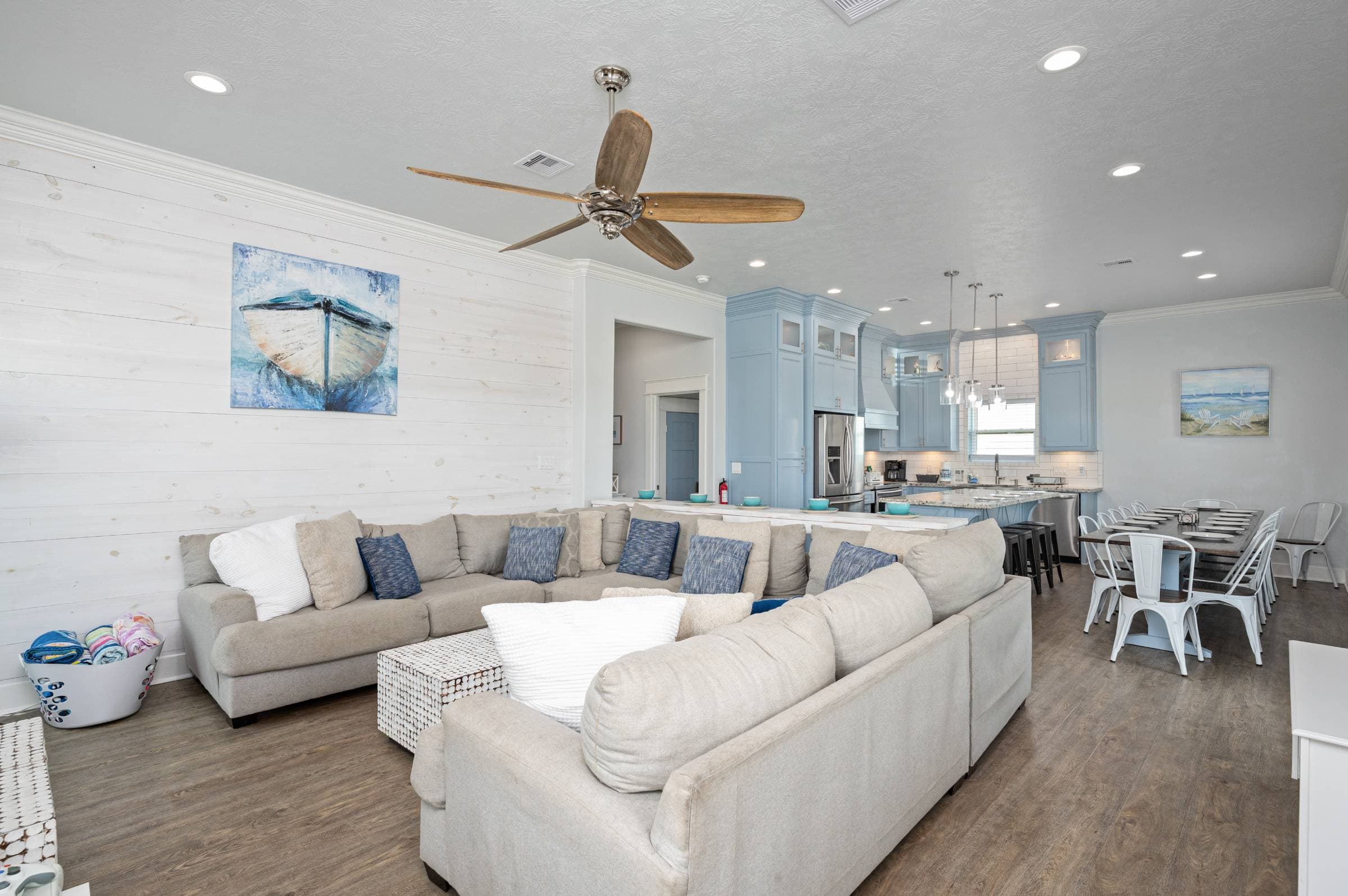 Spacious open-concept living area with a large sectional, coastal décor, and nearby access to the fully stocked kitchen and custom-made dining table—perfect for gathering and entertaining with your group.
